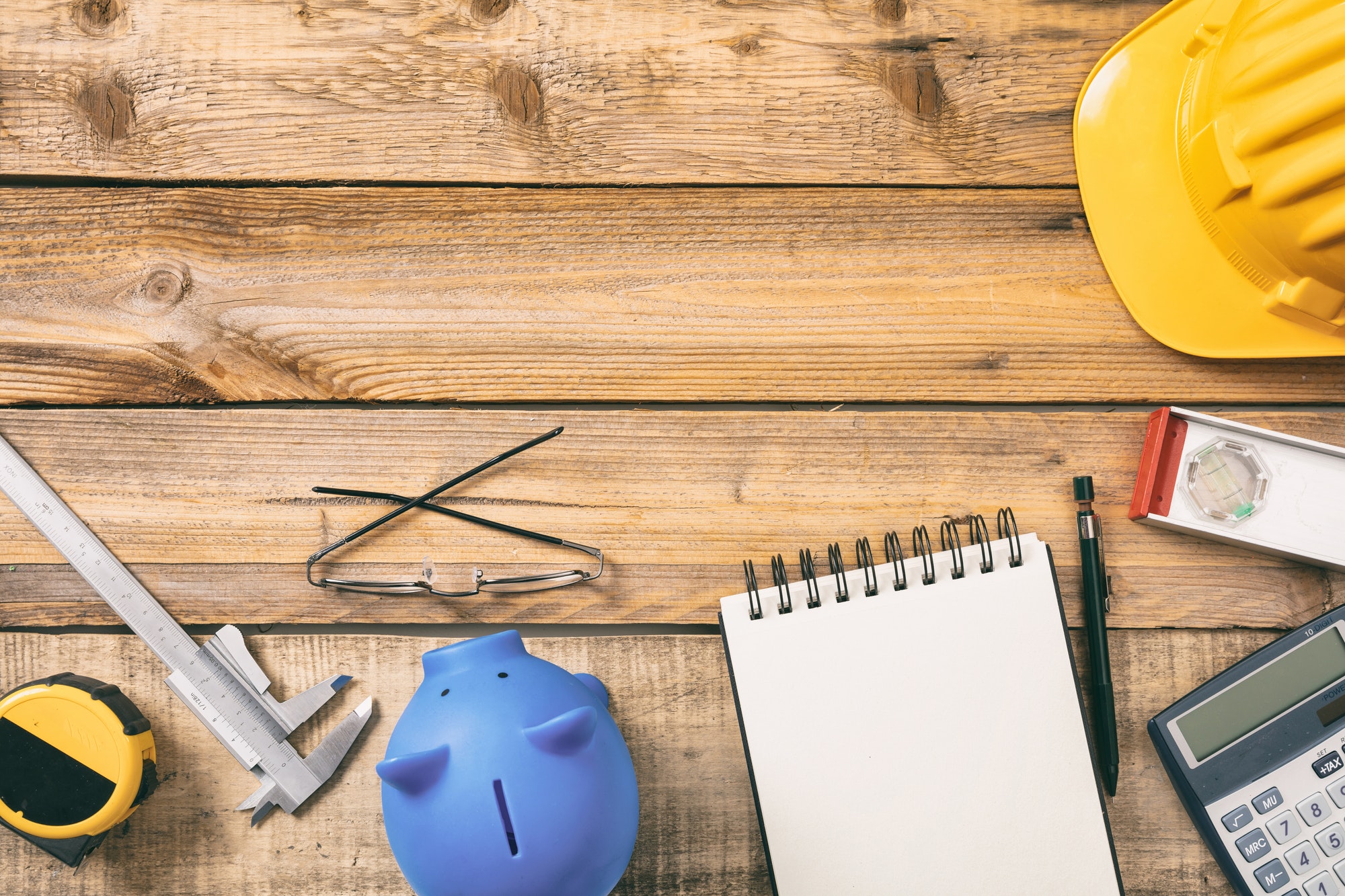 Project construction cost. Piggy bank, calculator and engineering equipment on a wooden desk